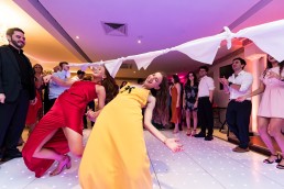 two wedding guests in dresses do an impromptu limbo on the dance floor.