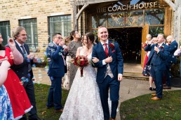 Bride and groom walk between two rows of their guests as they blow bubbles at them