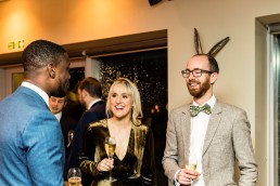 three wedding guests smile, one of them appears to have rabbit ears growing out of their head due to clever photographic composition.