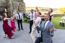 wedding guests dance outside at Danby Castle, with arms in the air