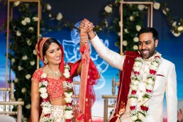hindu man and woman smiling and holding hands after getting married in front of a blue screen