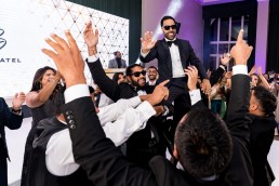 groom in sunglasses is hoisted onto his friends' shoulders on a dance floor. Everyone is wearing tuxedos.