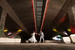 bride twirls her white dress as she dances with her groom underneath a subway. There are different coloured lights and use of off-camera flash from the side to create a dramatic lighting scene