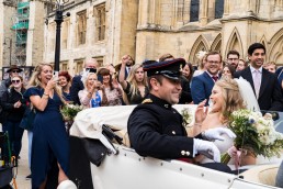 military wedding at york minster, the couple leave in their wedding car as guests cheer