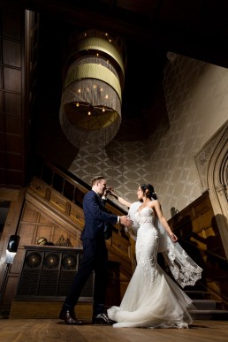 bride in white dress and groom in navy suit dance underneath a chandelier at Hampton Manor