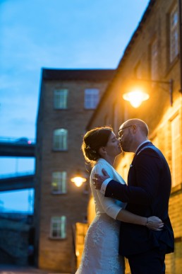 dusky blue skies and street lights illuminate newly weds as they kiss