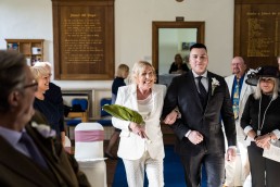 bride walks down the aisle to meet her groom escorted by her son