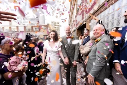 pink orange and white confetti file the frame as two newlyweds walk outside Trafalgar Warehouse