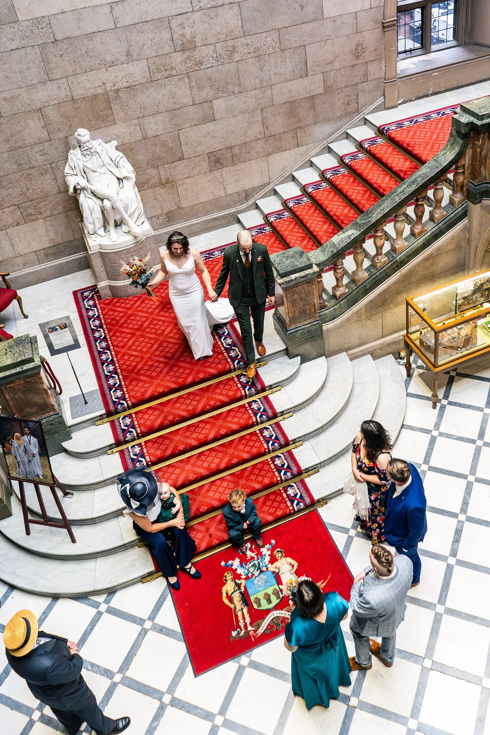 Couple walking down the grand staircase at Sheffield Town Hall after their wedding ceremony, guests waiting below, shot from above