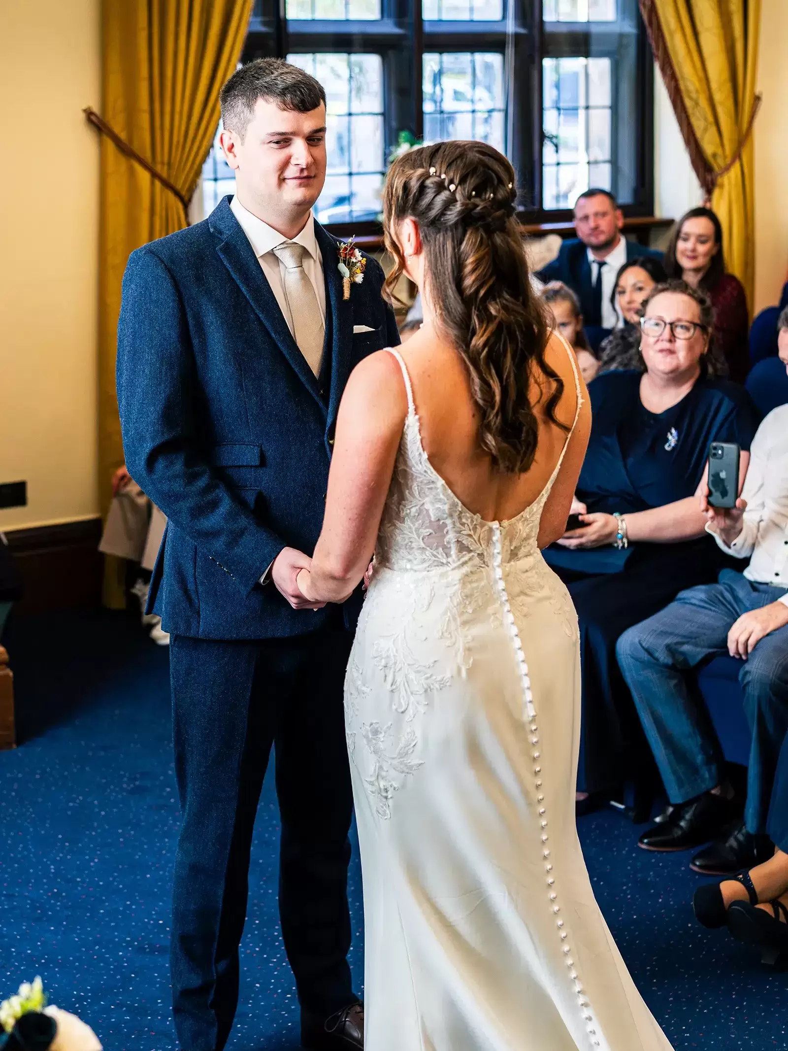 Bride and groom holding hands during wedding ceremony in the Hallam Room at Sheffield Town Hall, groom smiling